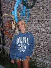 Load image into Gallery viewer, Person wearing a blue hoodie with text, standing next to a bicycle against a textured wall.