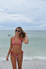 Load image into Gallery viewer, Woman in a red bikini standing on a beach with clear blue sky and ocean.