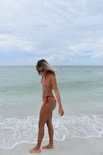 Load image into Gallery viewer, Woman in a red bikini standing on a beach with clear blue water.