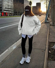 Load image into Gallery viewer, Person wearing a white sweater, black leggings, and white sneakers on a city street.