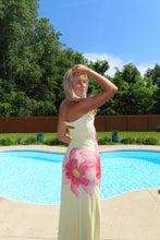 Load image into Gallery viewer, Woman in a floral dress standing by a pool with trees in the background