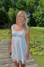 Load image into Gallery viewer, Woman in a light blue dress standing on a wooden dock by a pond with lily pads and trees in the background.