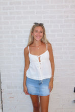 Load image into Gallery viewer, Woman wearing a white top and denim skirt standing against a light brick wall.