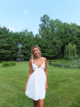 Load image into Gallery viewer, Woman in a white dress standing in a grassy field with trees and a windmill in the background.