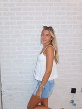 Load image into Gallery viewer, Woman lying on a textured white surface wearing a white top and denim shorts.