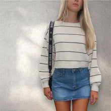 Load image into Gallery viewer, A person wearing a cropped striped beige and black sweater and a pair of denim shorts.