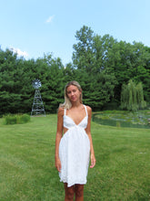 Load image into Gallery viewer, Woman in a white dress standing in a grassy field with trees and a windmill in the background.
