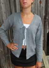 Load image into Gallery viewer, Person wearing a gray cardigan over a white top and black skirt against a wooden background