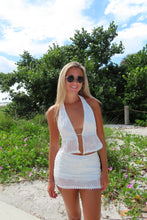 Load image into Gallery viewer, Woman in a white dress standing outdoors with trees and flowers in the background