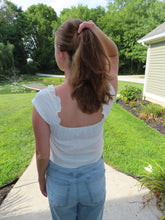 Load image into Gallery viewer, Person wearing a white top and blue jeans standing on a sidewalk with greenery in the background