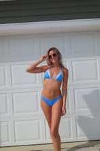 Load image into Gallery viewer, Woman in a blue bikini standing against a white garage door.