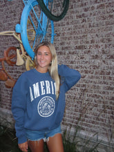 Load image into Gallery viewer, Person wearing a blue hoodie with a logo, standing next to a bicycle on a textured ground.