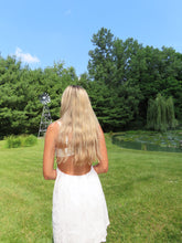 Load image into Gallery viewer, Person in a white dress standing on grass with trees and a windmill in the background