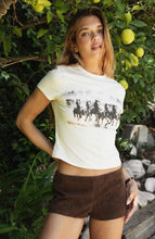 Load image into Gallery viewer, Woman wearing a white t-shirt with graphic design and brown shorts standing outdoors.