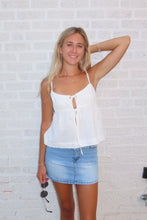 Load image into Gallery viewer, Woman wearing a white top and denim skirt against a white brick wall.