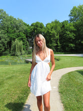 Load image into Gallery viewer, Woman in a white dress standing in a park with trees and grass.