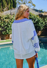 Load image into Gallery viewer, Woman wearing a light gray and blue sweater by a poolside