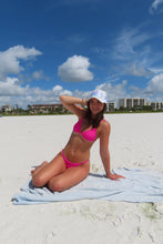Load image into Gallery viewer, Woman in pink bikini and white cap on a sandy beach with blue sky and clouds.