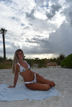 Load image into Gallery viewer, Woman in a white bikini sitting on a towel at the beach with palm trees and blue sky.