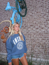Load image into Gallery viewer, Person wearing a blue sweatshirt with a logo on a textured floor