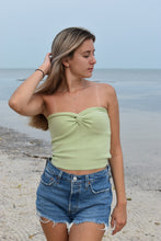 Load image into Gallery viewer, A woman wearing a light green twisted knit top and blue denim shorts, standing by the beach.