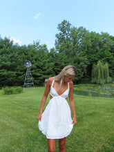Load image into Gallery viewer, Woman in a white dress standing on grass with trees and a windmill in the background