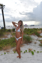 Load image into Gallery viewer, Woman in a white bikini on a sandy beach with palm trees in the background