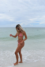 Load image into Gallery viewer, Woman in a pink bikini standing on a beach with clear water.