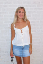 Load image into Gallery viewer, Woman wearing a white top and denim skirt against a white brick wall.
