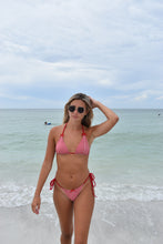 Load image into Gallery viewer, Woman in a red bikini standing on a beach with clear blue water.