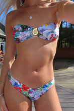 Load image into Gallery viewer, Person wearing a colorful floral bikini with a decorative bow on a wooden deck.