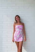Load image into Gallery viewer, Woman wearing a pink and white patterned strapless dress against a white tiled wall.