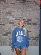 Load image into Gallery viewer, Person wearing a blue sweatshirt with 'American' text on a brick-patterned floor.
