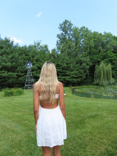 Load image into Gallery viewer, Person wearing a white dress standing in a grassy field with trees and a windmill in the background.