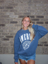 Load image into Gallery viewer, Person wearing a blue sweatshirt with a logo against a brick wall.