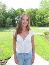 Load image into Gallery viewer, Woman in a white blouse and denim shorts standing outdoors with greenery in the background