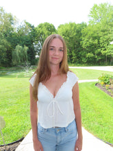 Load image into Gallery viewer, Woman in a white top and blue shorts standing outdoors with greenery in the background