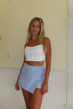 Load image into Gallery viewer, Woman wearing a white top and blue striped shorts standing against a plain wall.