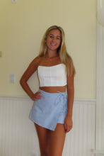 Load image into Gallery viewer, Woman wearing a white top and blue shorts standing in a room with a neutral wall and window blinds.