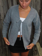 Load image into Gallery viewer, Person wearing a gray cardigan over a white top and black shorts against a wooden background