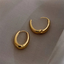 Load image into Gallery viewer, A pair of gold hoop earrings with a high shine finish displayed on a textured surface.
