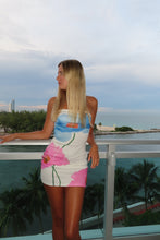 Load image into Gallery viewer, Woman in a colorful dress standing by a pool with palm trees in the background