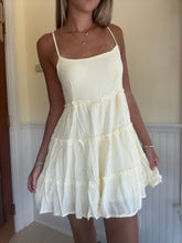 Load image into Gallery viewer, A woman wearing a yellow A-line dress with ruffle details at the neckline and hem, paired with a white strapless top.
