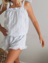 Load image into Gallery viewer, A woman wearing a light blue and white striped halter top and matching shorts, captured in motion against a plain light gray wall.
