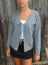 Load image into Gallery viewer, Person wearing a gray cardigan over a white top and black shorts against a wooden fence background
