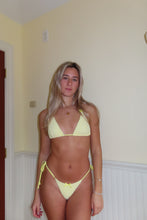 Load image into Gallery viewer, Woman wearing a yellow bikini standing in a room with beige walls.
