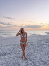 Load image into Gallery viewer, Woman in a bikini standing on a beach with a sunset in the background
