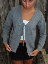 Load image into Gallery viewer, Person wearing a gray cardigan over a white top and black shorts against a wooden background
