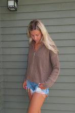 Load image into Gallery viewer, Woman wearing a brown knitted sweater and denim shorts standing against a gray wall.
