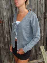 Load image into Gallery viewer, Woman wearing a gray cardigan over a white top and black shorts against a wooden fence background
